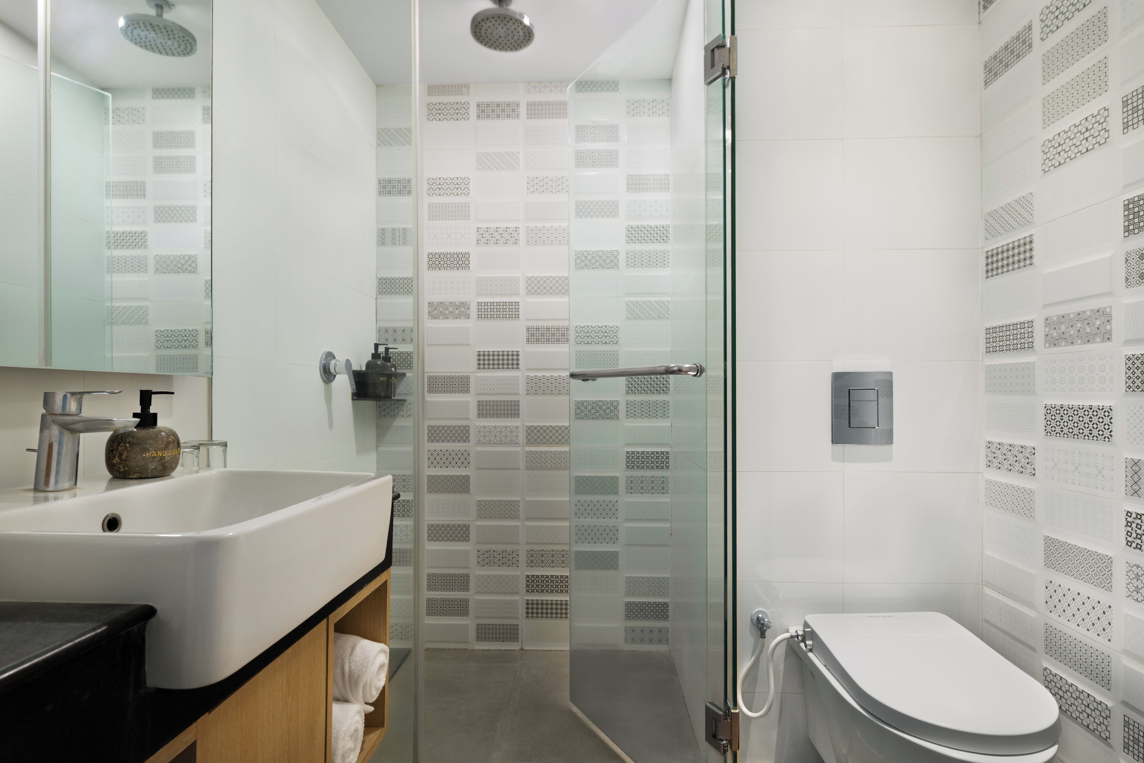 A modern bathroom with a glass-enclosed shower, a white sink with a soap dispenser, and a toilet.