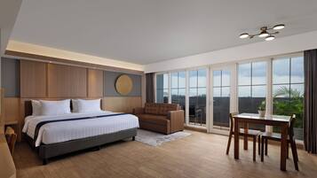 A modern hotel room with a large bed, a sofa, a dining table, and a balcony with a view.