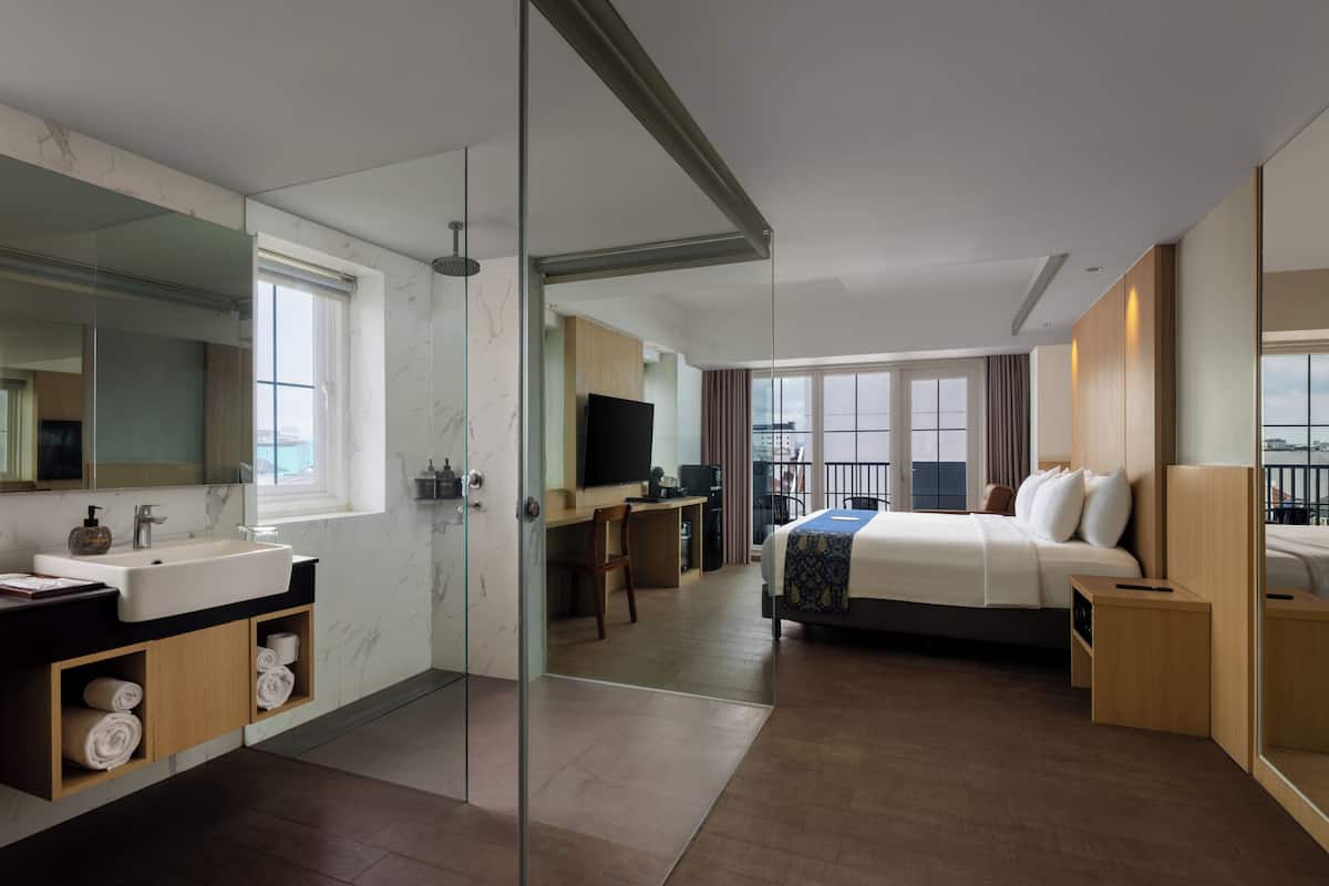 A modern hotel room with a large bed, a desk, a bathroom with a sink and mirror, and a balcony with a view.