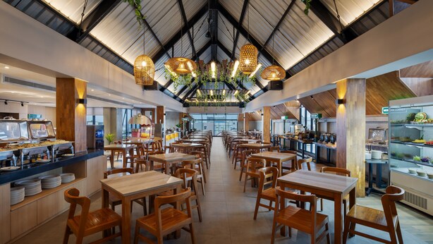 A spacious restaurant with high ceilings, wooden tables and chairs, and hanging light fixtures. - Aveta Hotel Malioboro (Yogyakarta)