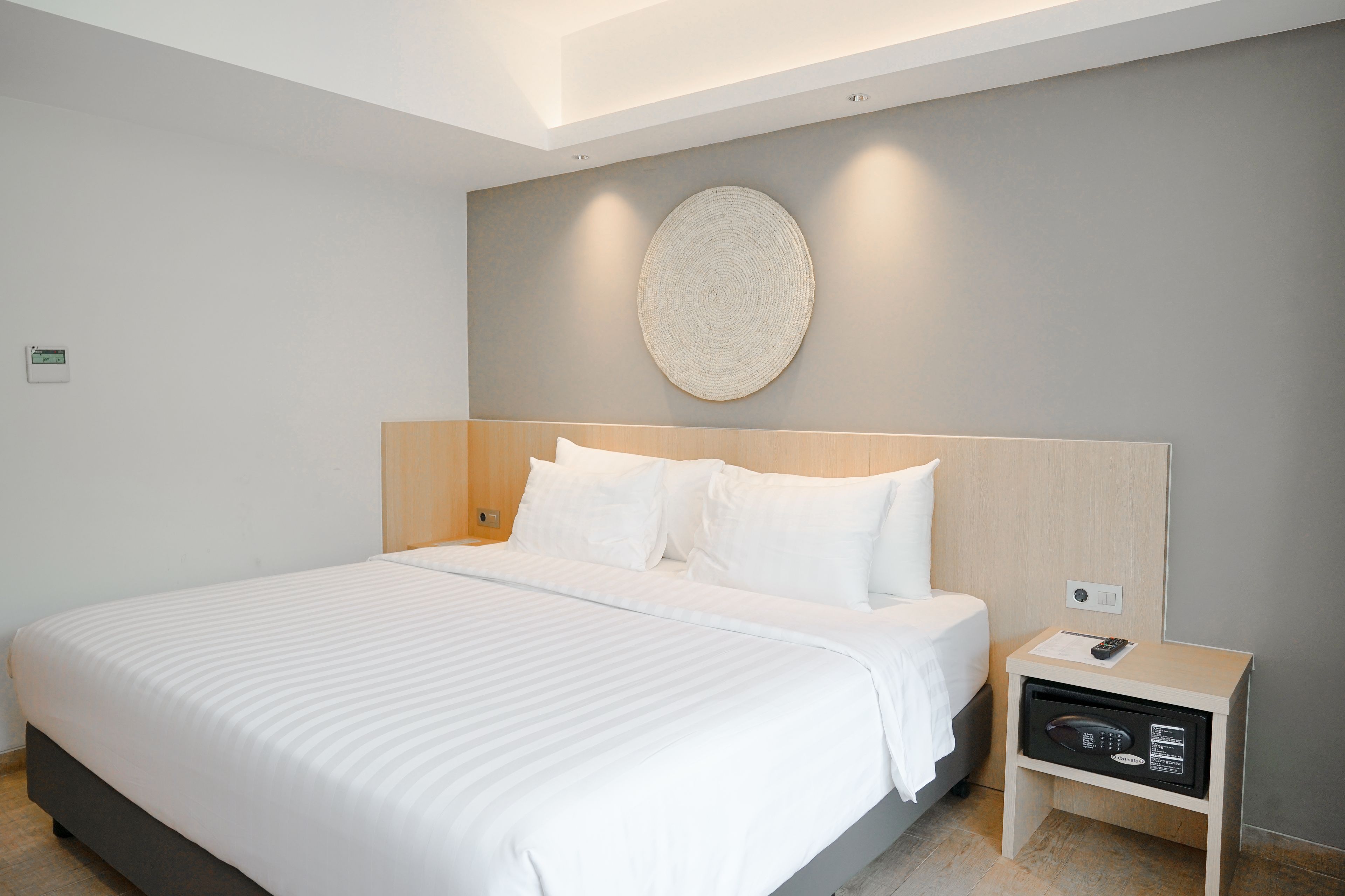 Een moderne hotelkamer met een groot bed, een nachtkastje met een afstandsbediening, en een decoratief object aan de muur.