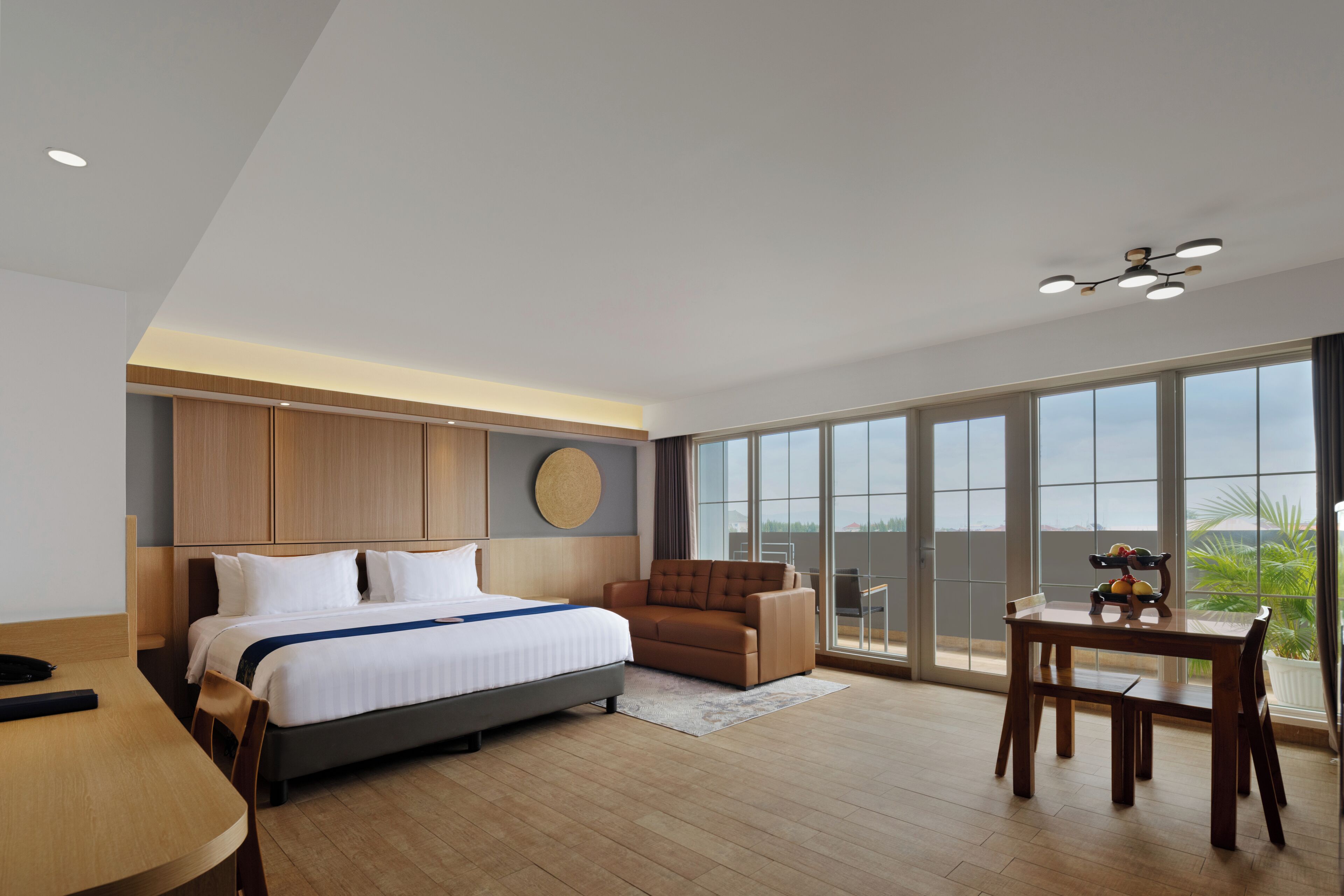 A modern hotel room with a large bed, a sofa, a dining table, and a balcony with a view.