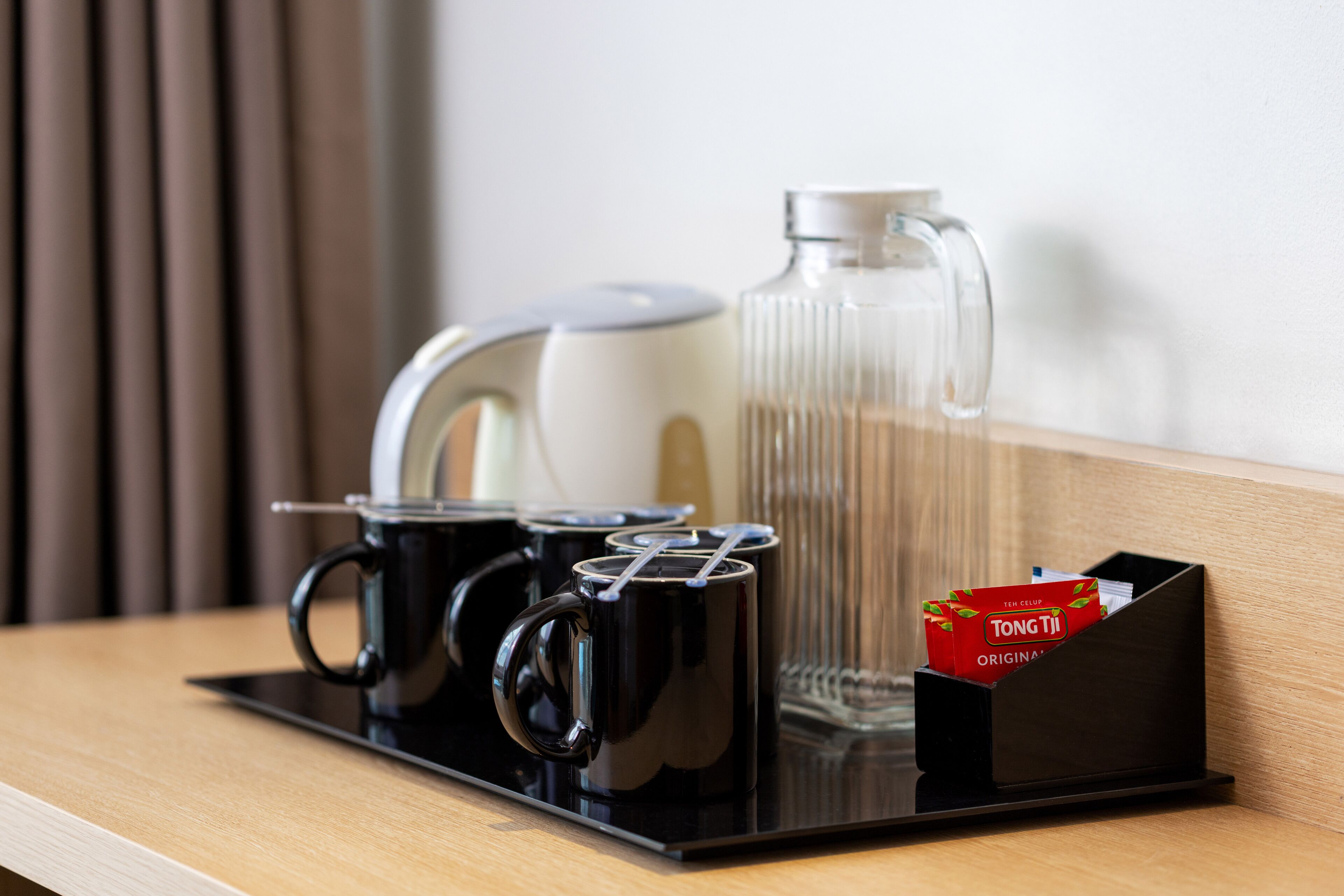 Una estación de café con una cafetera, dos tazas negras, una jarra de vidrio y una caja de té Tong Tai.