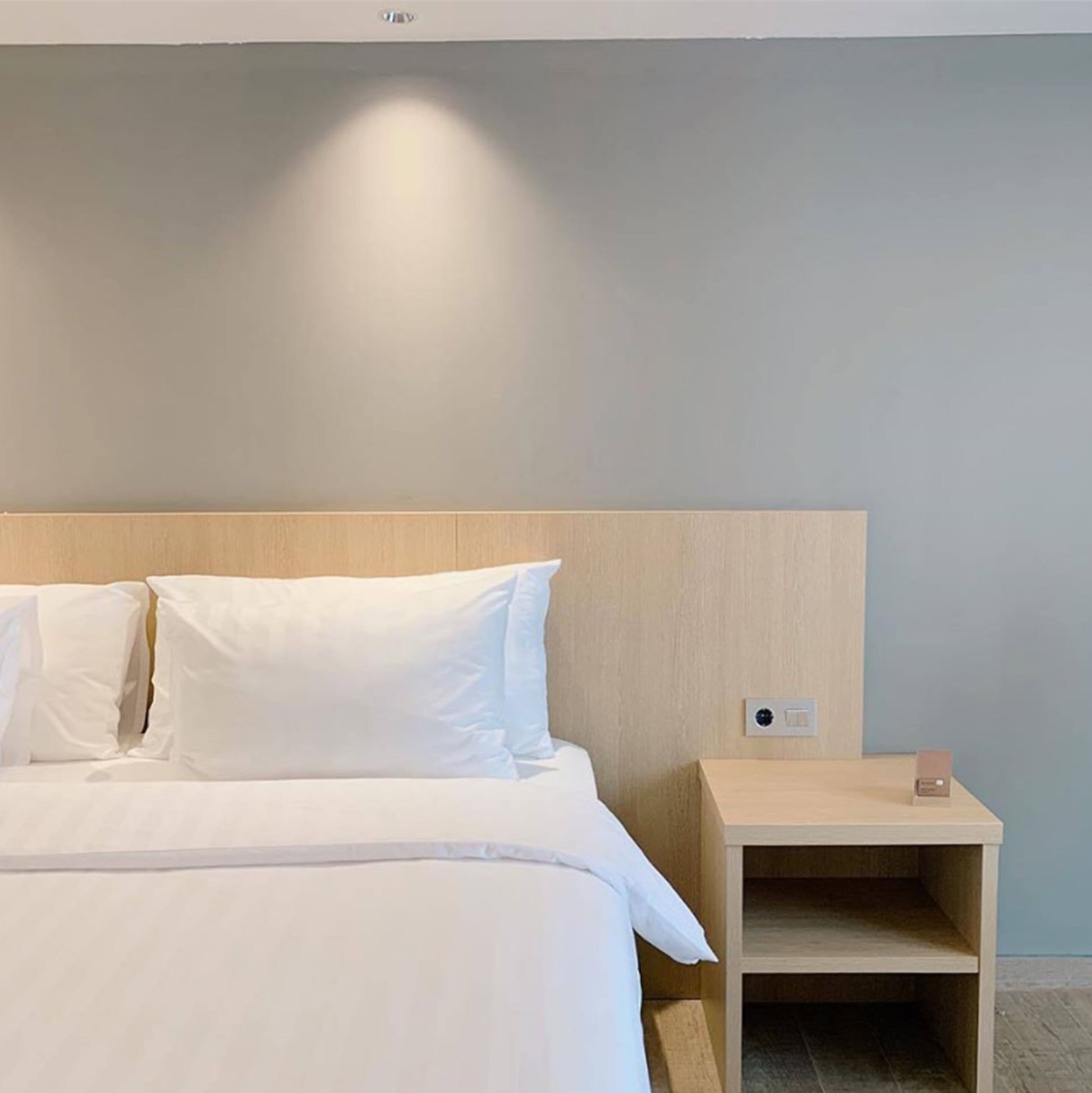 A hotel room with a bed, white bedding, a wooden headboard, and a nightstand with a lamp.