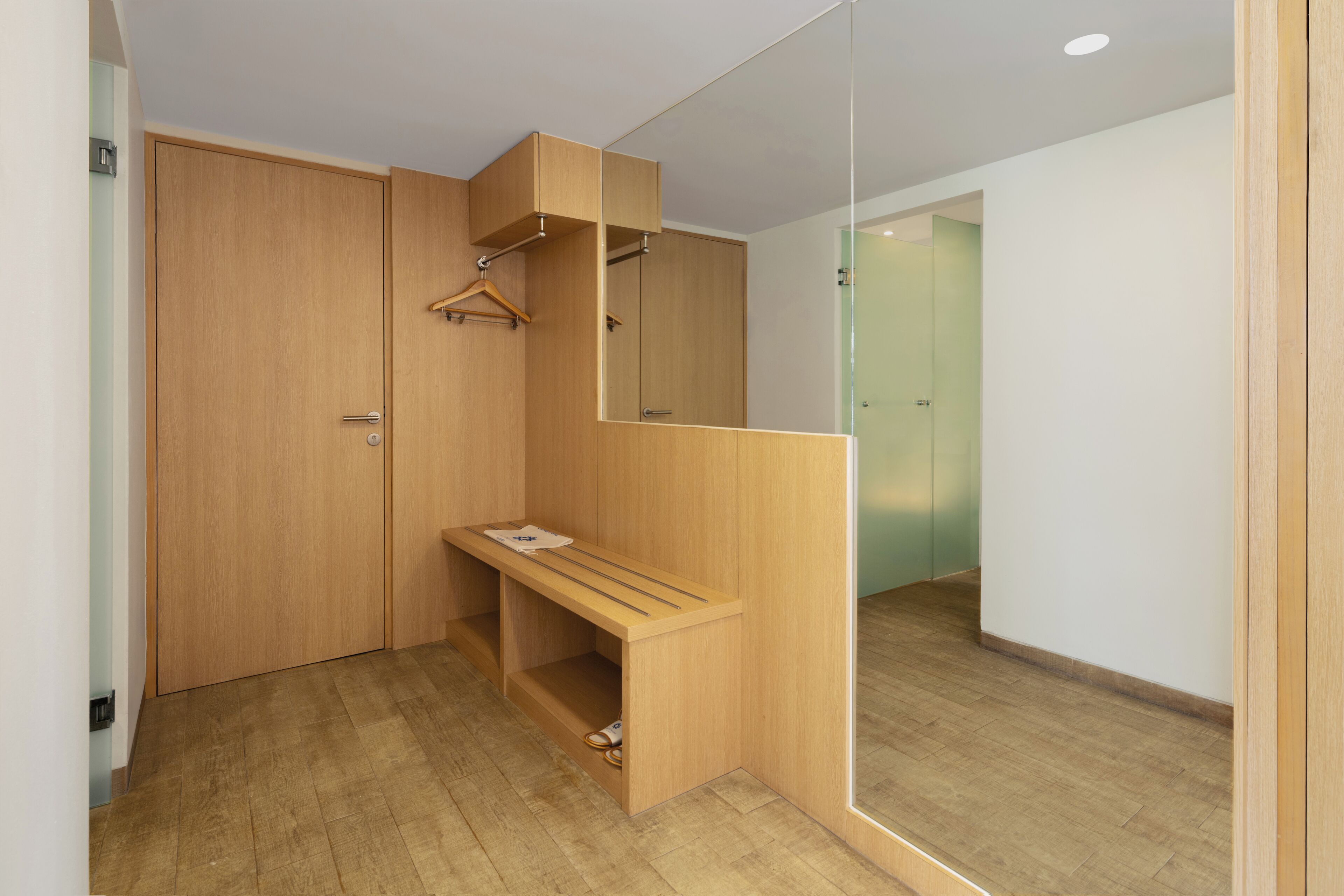 Una habitación moderna con suelo de madera, un banco, un espejo y un armario de madera.