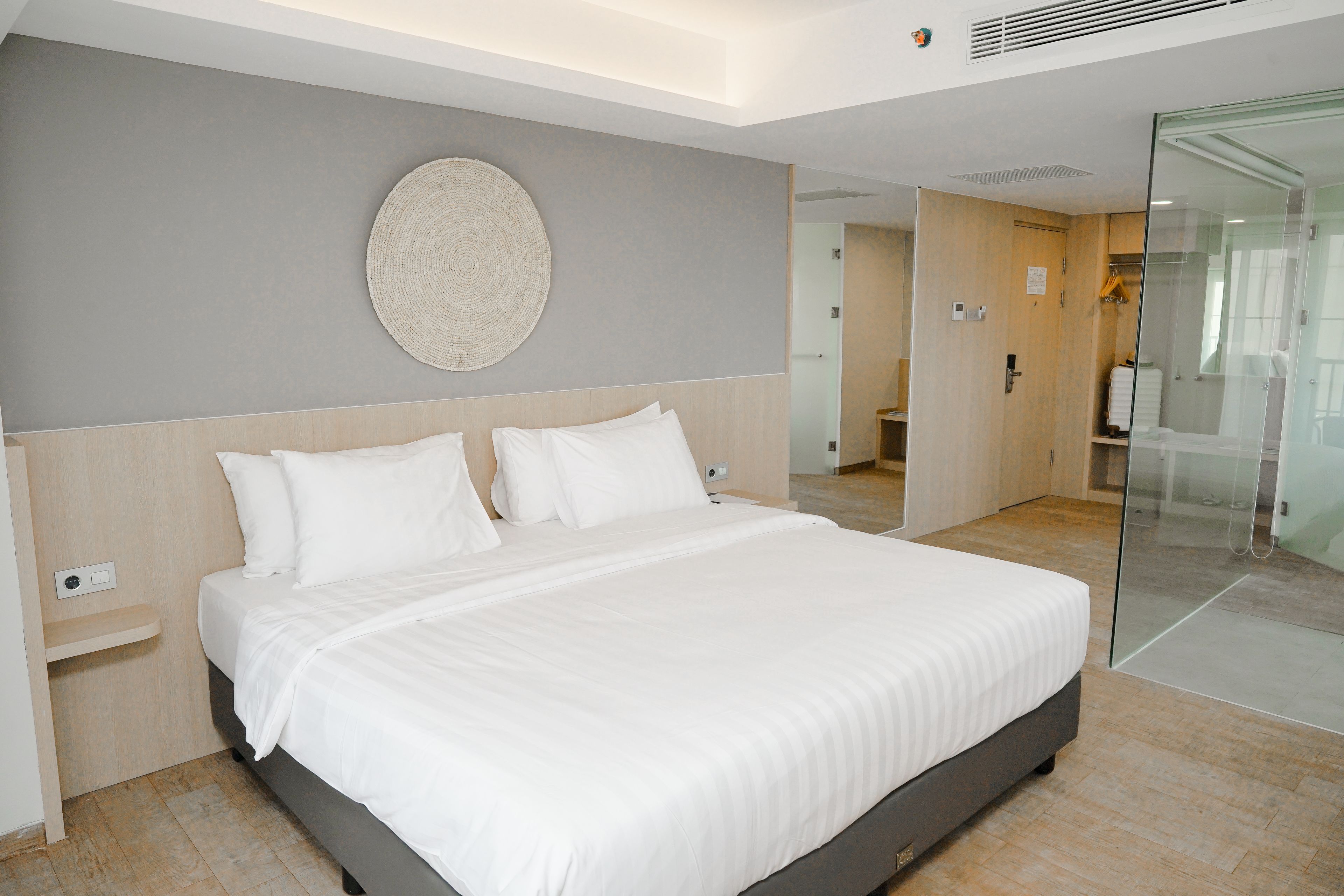 A modern hotel room with a large bed, a round wall decoration, and a glass partition.