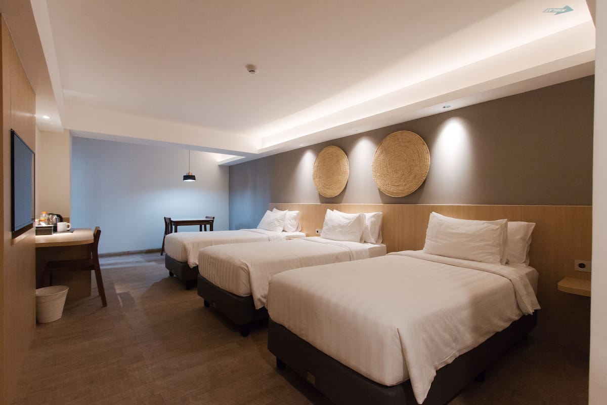 A hotel room with three beds, a desk, and a chair.