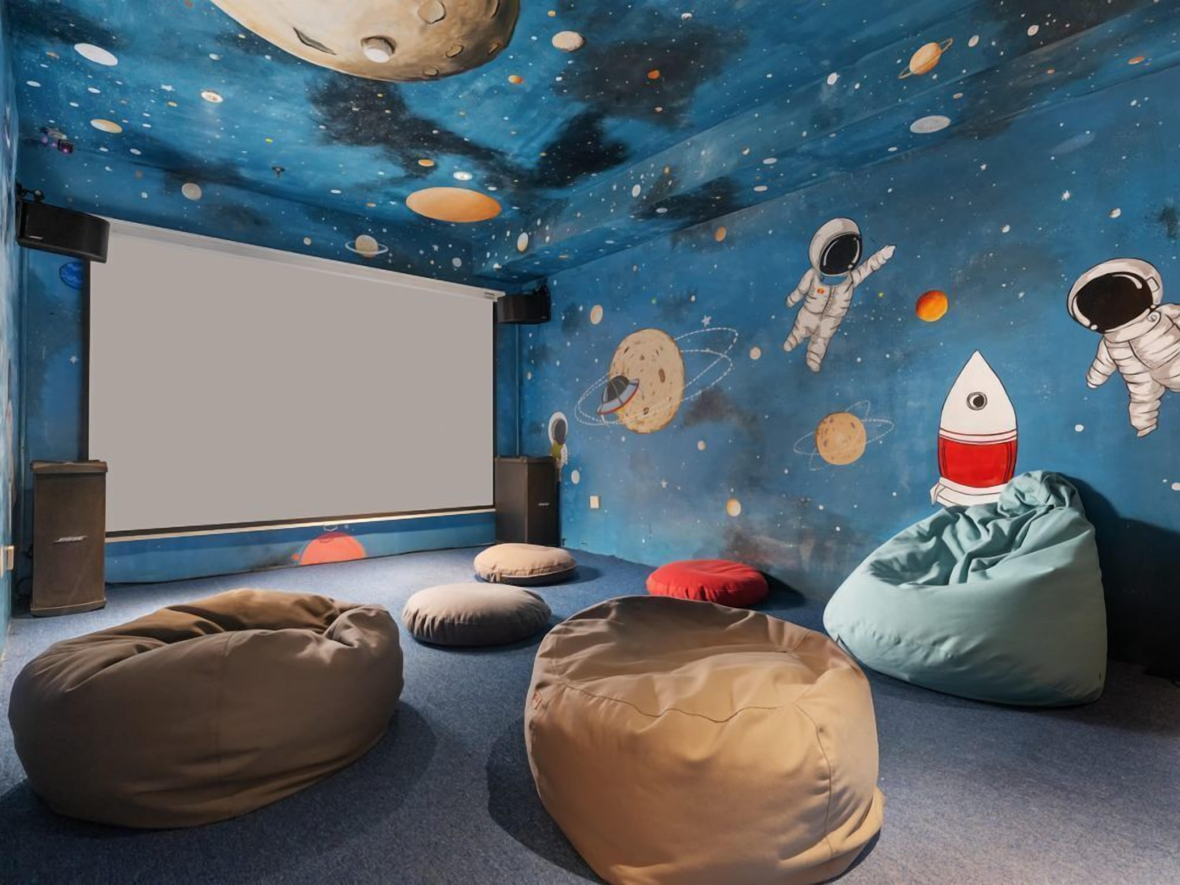 Una habitación con un mural con tema espacial, pufs y una pantalla de proyector.