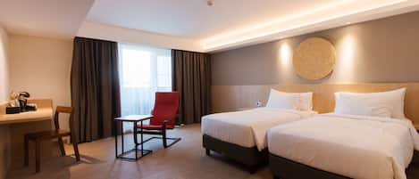 A hotel room with two beds, a desk, a chair, and a large window with curtains.