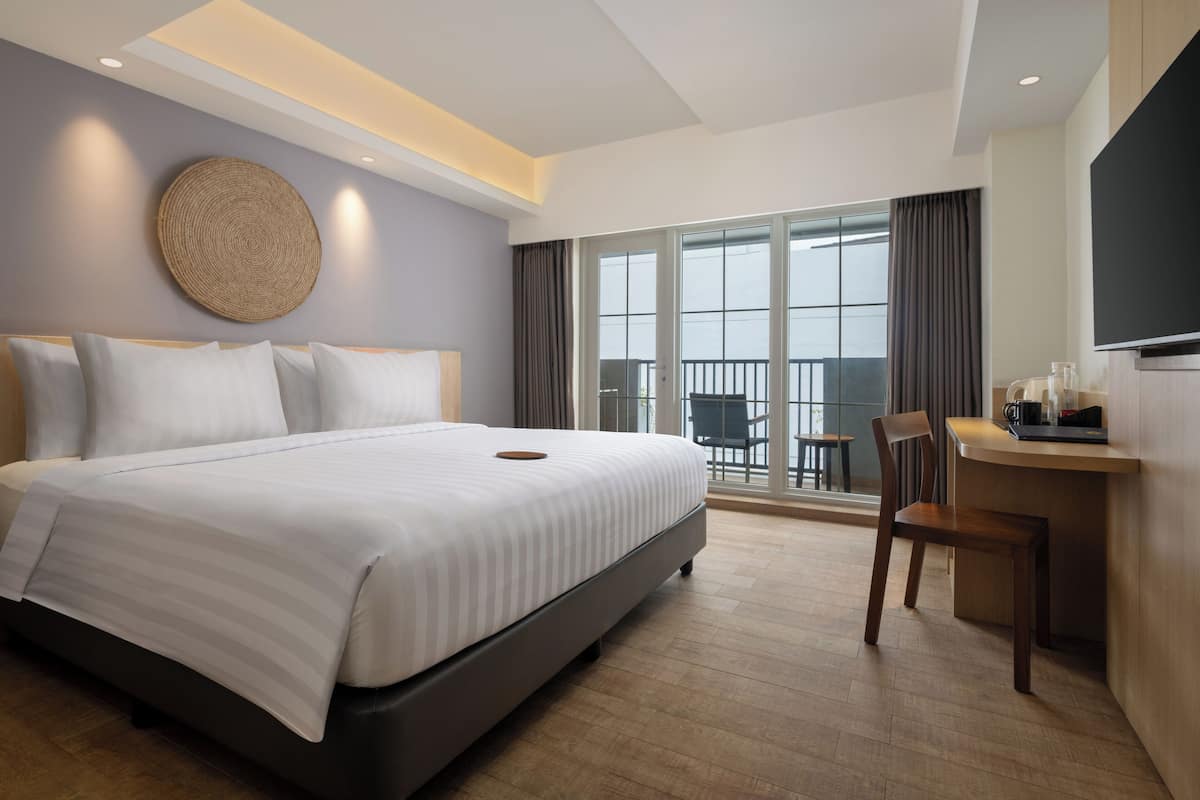 A modern hotel room with a large bed, a desk, and a balcony with a view.