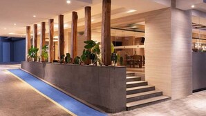 A modern lobby with a central column, potted plants, and a blue carpet leading to a staircase. - Aveta Hotel Malioboro (Yogyakarta)