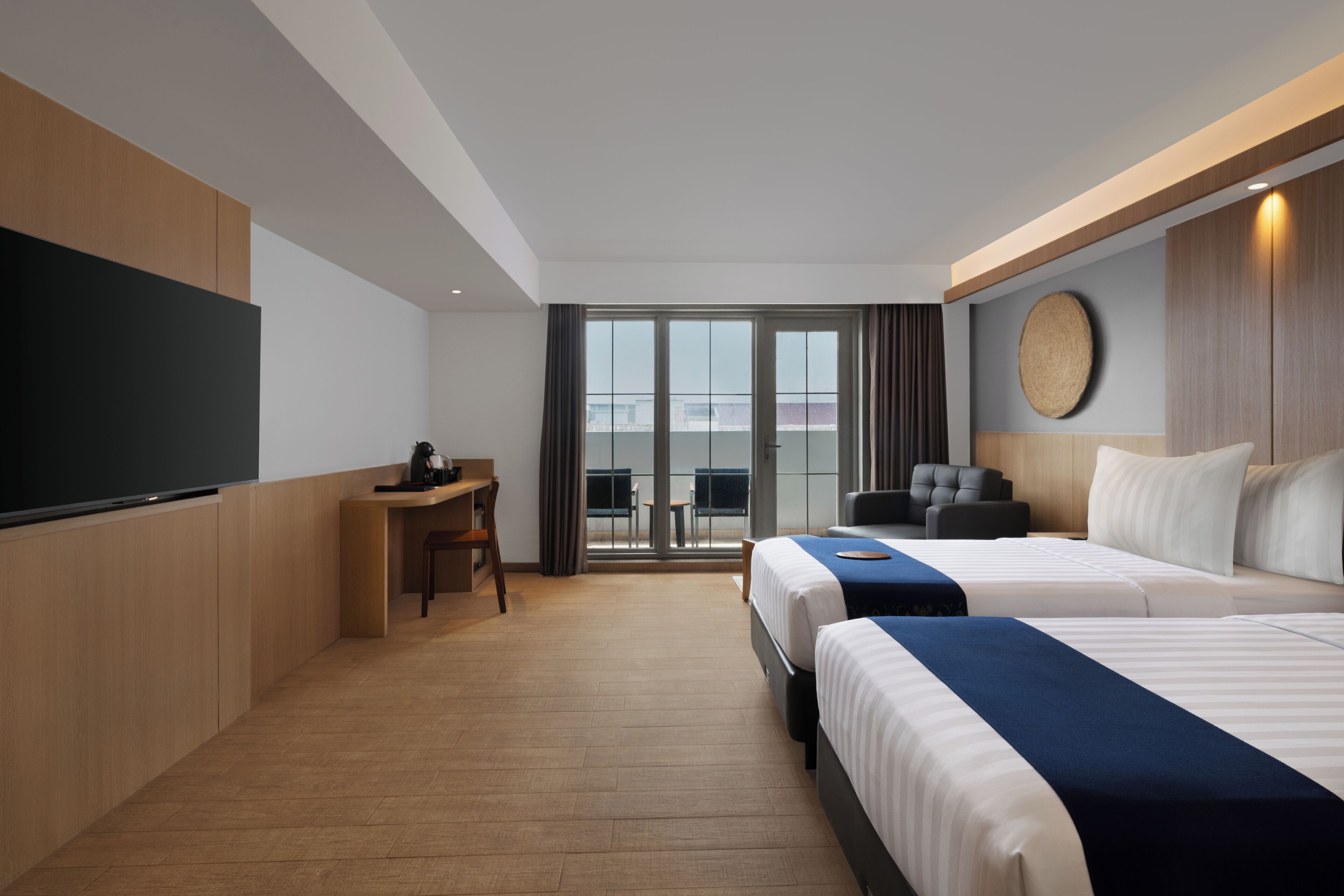 A hotel room with two beds, a desk, a TV, and a balcony with a view.