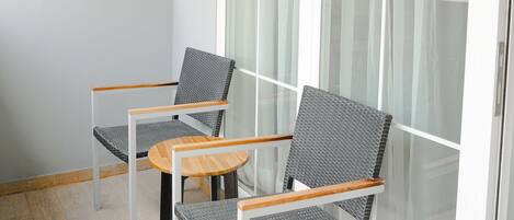 Un balcón con dos sillas, una mesa, puertas grandes de cristal y suelo de tonos claros.