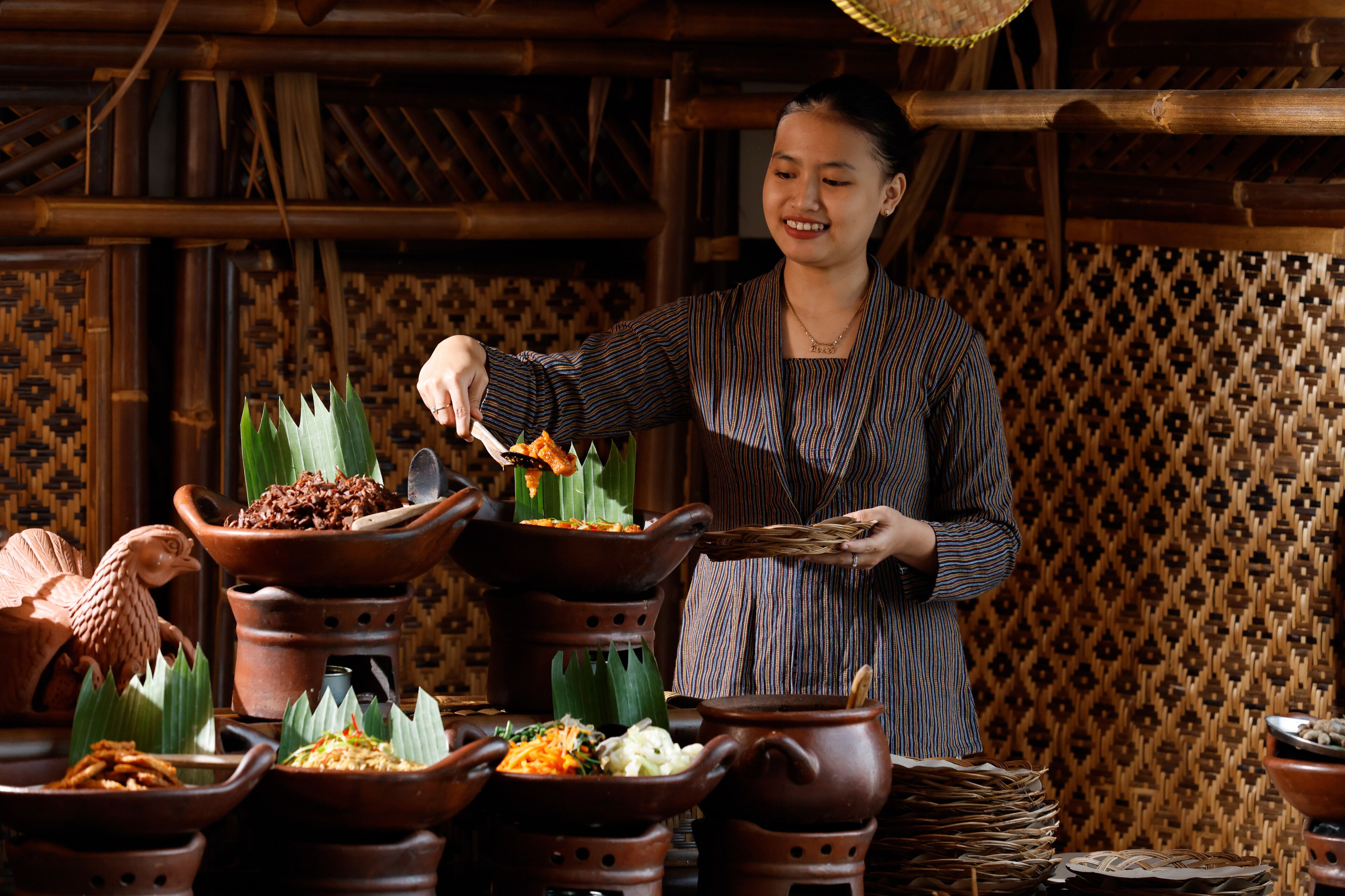 A person serving food from multiple clay pots on a woven mat.