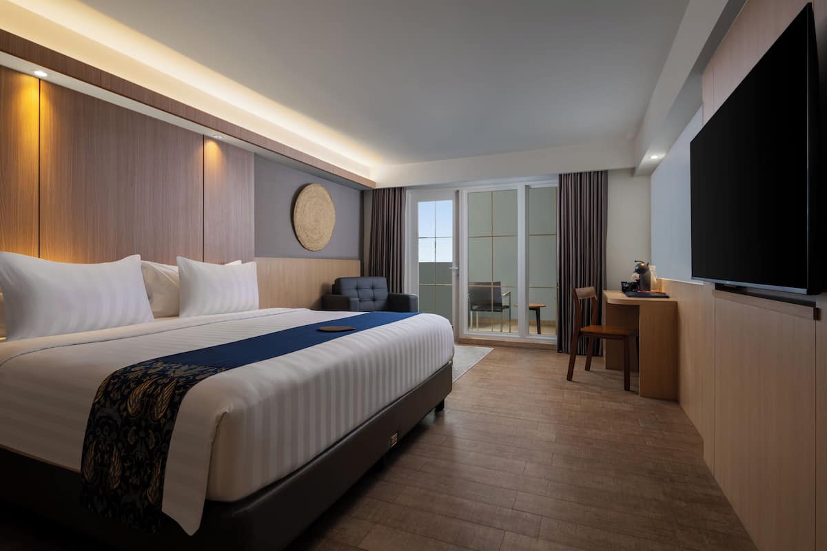 A hotel room with a large bed, a desk, a chair, and a TV.