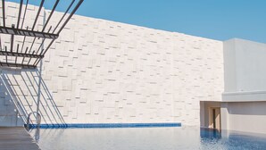 A swimming pool with a modern architectural design, featuring a geometric wall pattern and a clear blue sky. - Aveta Hotel Malioboro (Yogyakarta)