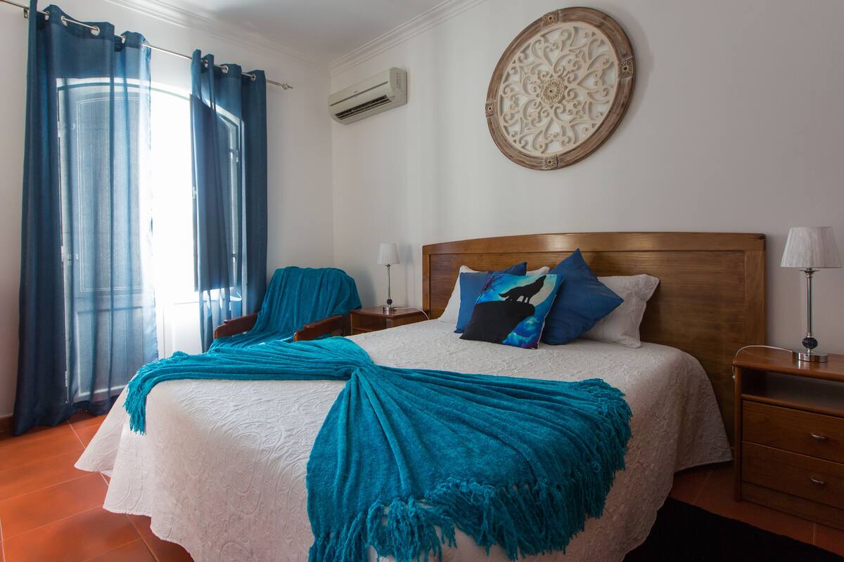 A neatly made bed with a blue blanket, a wooden headboard, and a decorative wall piece.