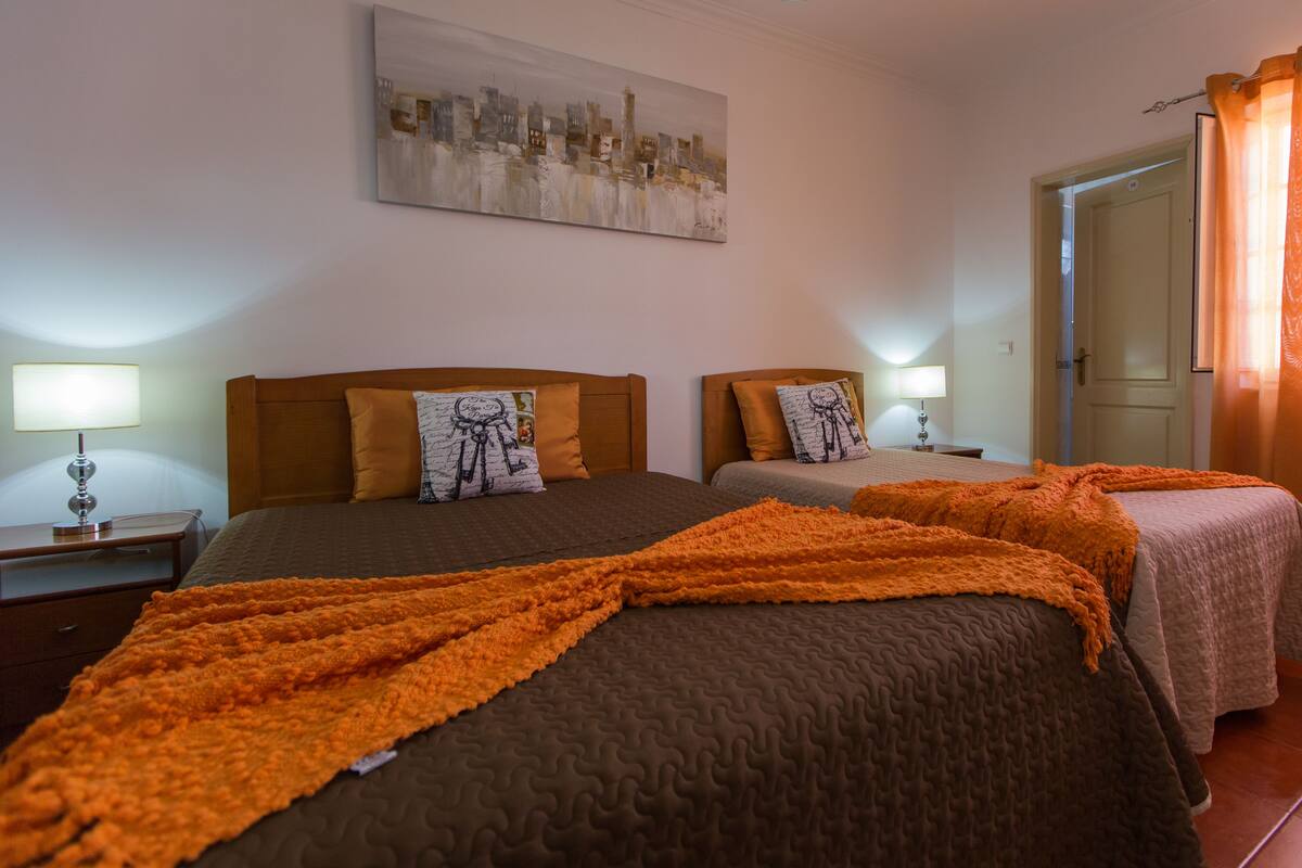A hotel room with two beds, a cityscape painting on the wall, and a door with a curtain.