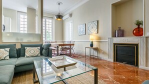 Ein modernes Wohnzimmer mit einem Glastisch, einer Couch mit gemusterten Kissen, einem Kamin und einem Essbereich mit einem roten Stuhl und Tisch.