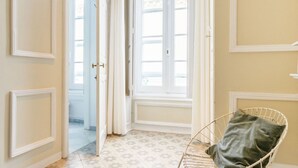 Ein Zimmer mit einem gemusterten Boden, einem weißen Stuhl mit Kissen und einer Tür zu einem weiteren Raum.