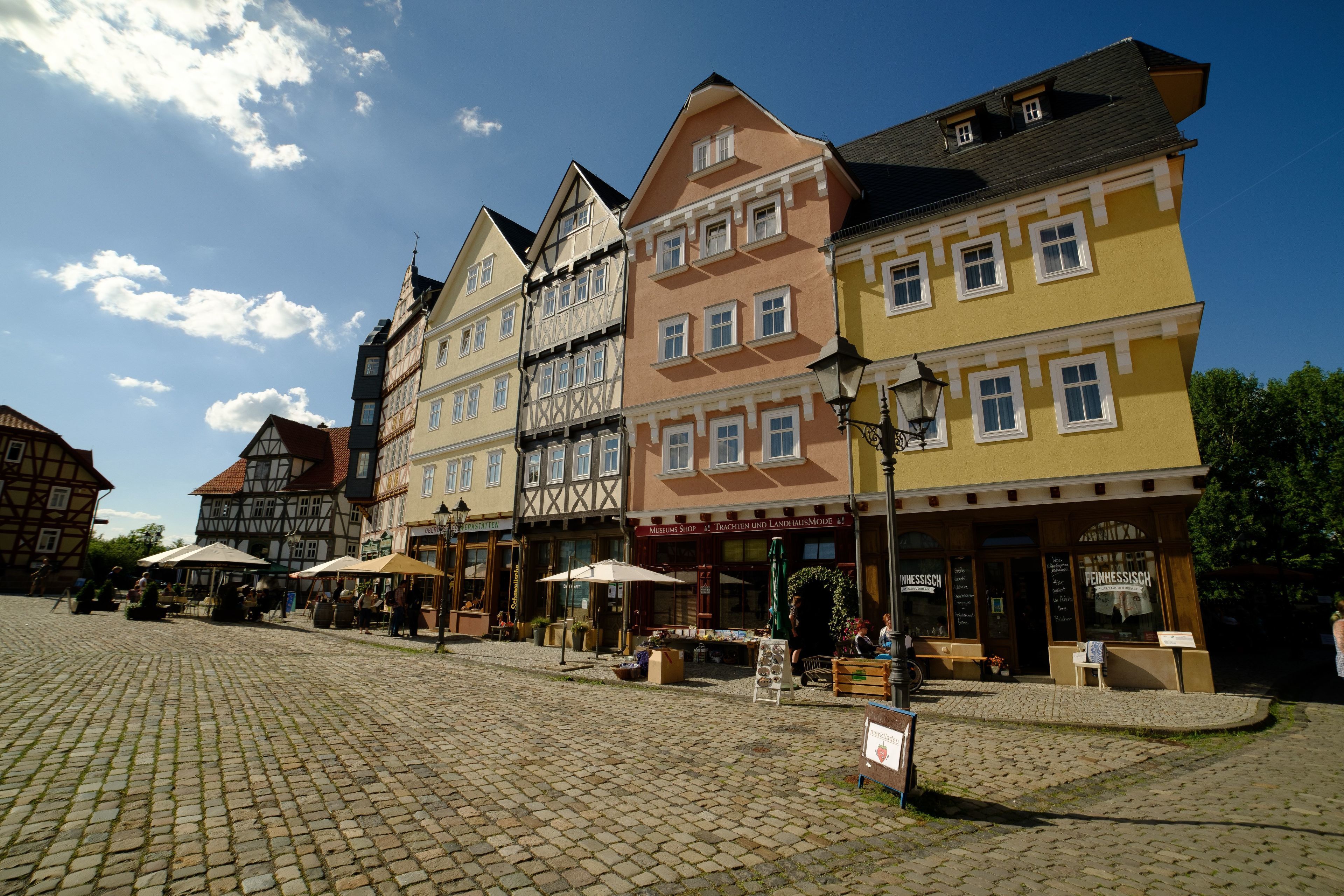 A cobblestone square with traditional European buildings, outdoor seating, and a clear blue sky.