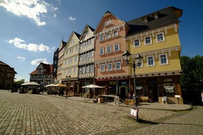 A cobblestone square with traditional European buildings, outdoor seating, and a clear blue sky. - Landhotel Zum Hessenpark (Neu-Anspach)