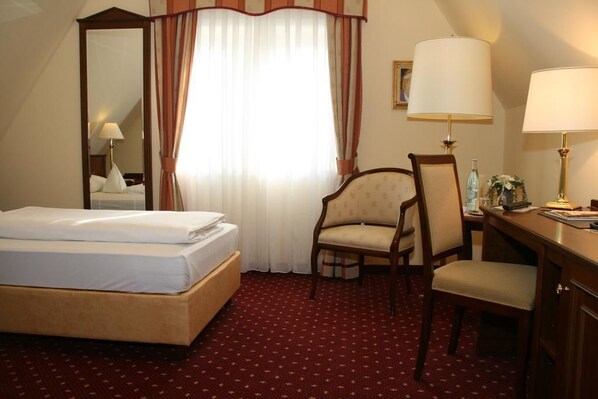 A hotel room with a bed, a desk, a chair, a lamp, and a mirror. - Landhotel Zum Hessenpark (Neu-Anspach)