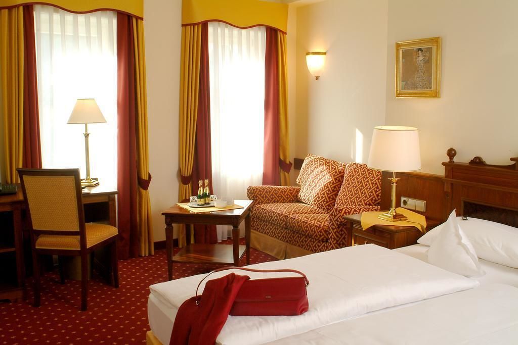 A hotel room with a bed, a desk, a chair, a sofa, and a lamp.