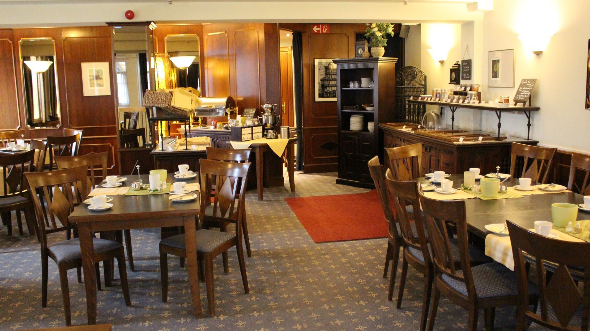 A dining area with wooden tables and chairs, a coffee station, and a bookshelf.