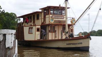 A large, multi-deck houseboat with a cabin and upper deck, docked at a pier.