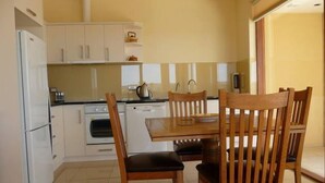 Une cuisine compacte avec des meubles blancs, une cuisinière, un four et un lave-vaisselle. On y trouve une table à manger en bois avec quatre chaises.