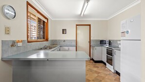 A modern kitchen with a central island, stainless steel appliances, and a window with blinds. - 1-44 Woodburn Street - (EVANS HEAD)