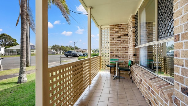 A balcony with a view of a street, a table with chairs, and a brick wall. - 1-44 Woodburn Street - (EVANS HEAD)