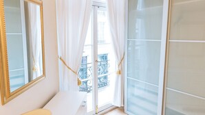Quarto de hotel com uma janela grande, um espelho, uma mesa de cabeceira e um guarda-roupa.