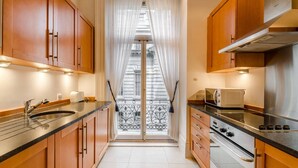 Uma cozinha estreita com armários de madeira, um fogão de aço inoxidável e uma janela com cortinas.