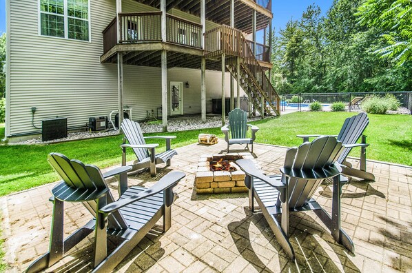 A patio with Adirondack chairs, a fire pit, and a wooden deck.
