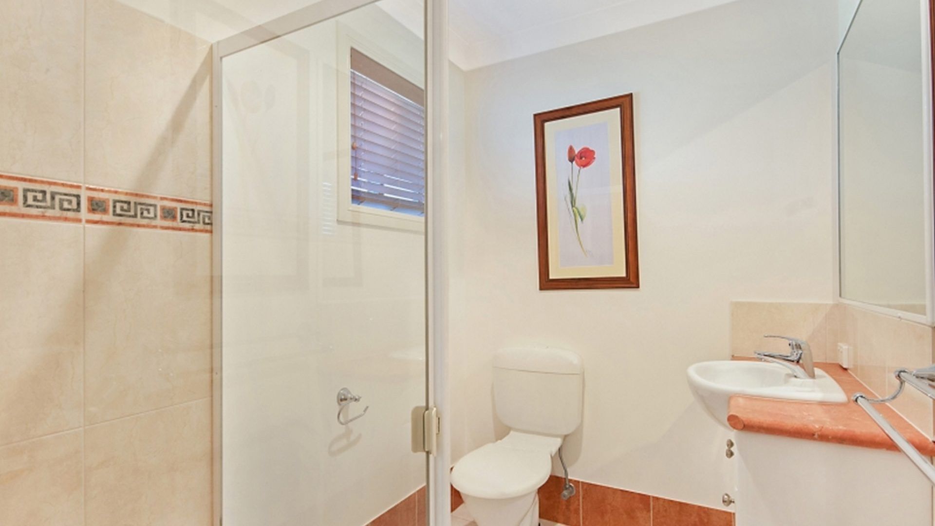 Un baño con cabina de ducha de vidrio, inodoro y lavamanos con espejo.