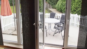 A sliding glass door leading to an outdoor patio with a white fence, a table, and two chairs. - Ferienwohnung Villa Am Golfplatz (Bad Harzburg)