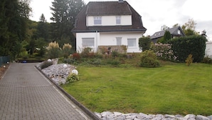 A paved pathway leading to a white house with a dark roof, surrounded by a well-maintained lawn and a stone wall. - Ferienwohnung Villa Am Golfplatz (Bad Harzburg)
