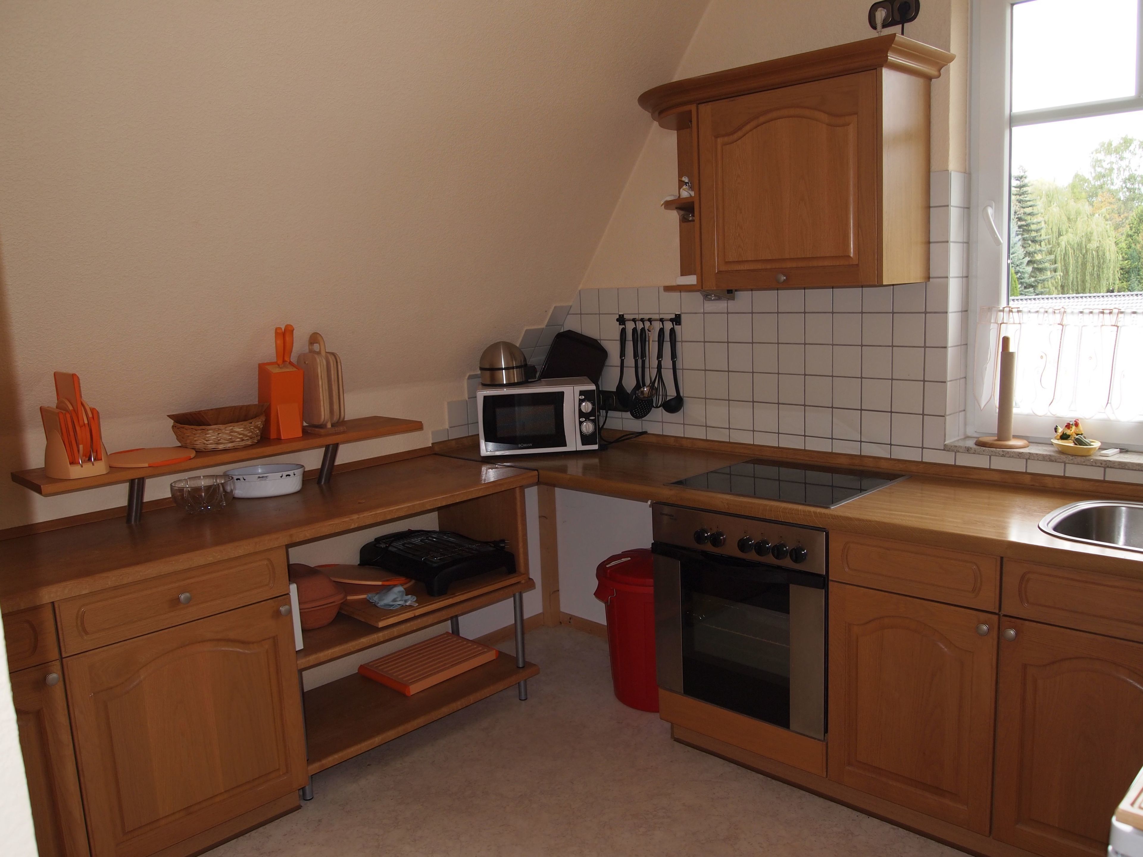 A compact kitchen with wooden cabinets, a microwave, a stove, and a sink.