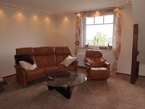 A living room with a brown leather sofa, a glass coffee table, and a leather armchair. - Ferienwohnung Villa Am Golfplatz (Bad Harzburg)
