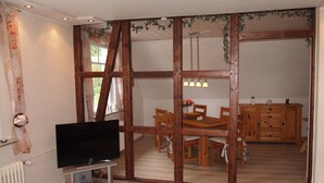 A living room with a flat-screen TV, wooden furniture, and a sliding door leading to a dining area. - Ferienwohnung Villa Am Golfplatz (Bad Harzburg)
