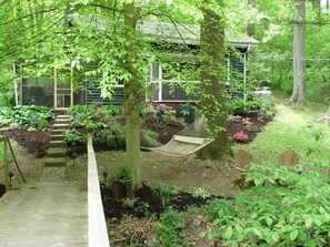 A wooden deck leading to a house surrounded by lush greenery and a hammock. - Wrightsville Cabin: Outdoor Fire Pit: Hammock by the creek: Long Level Marina (Wrightsville)