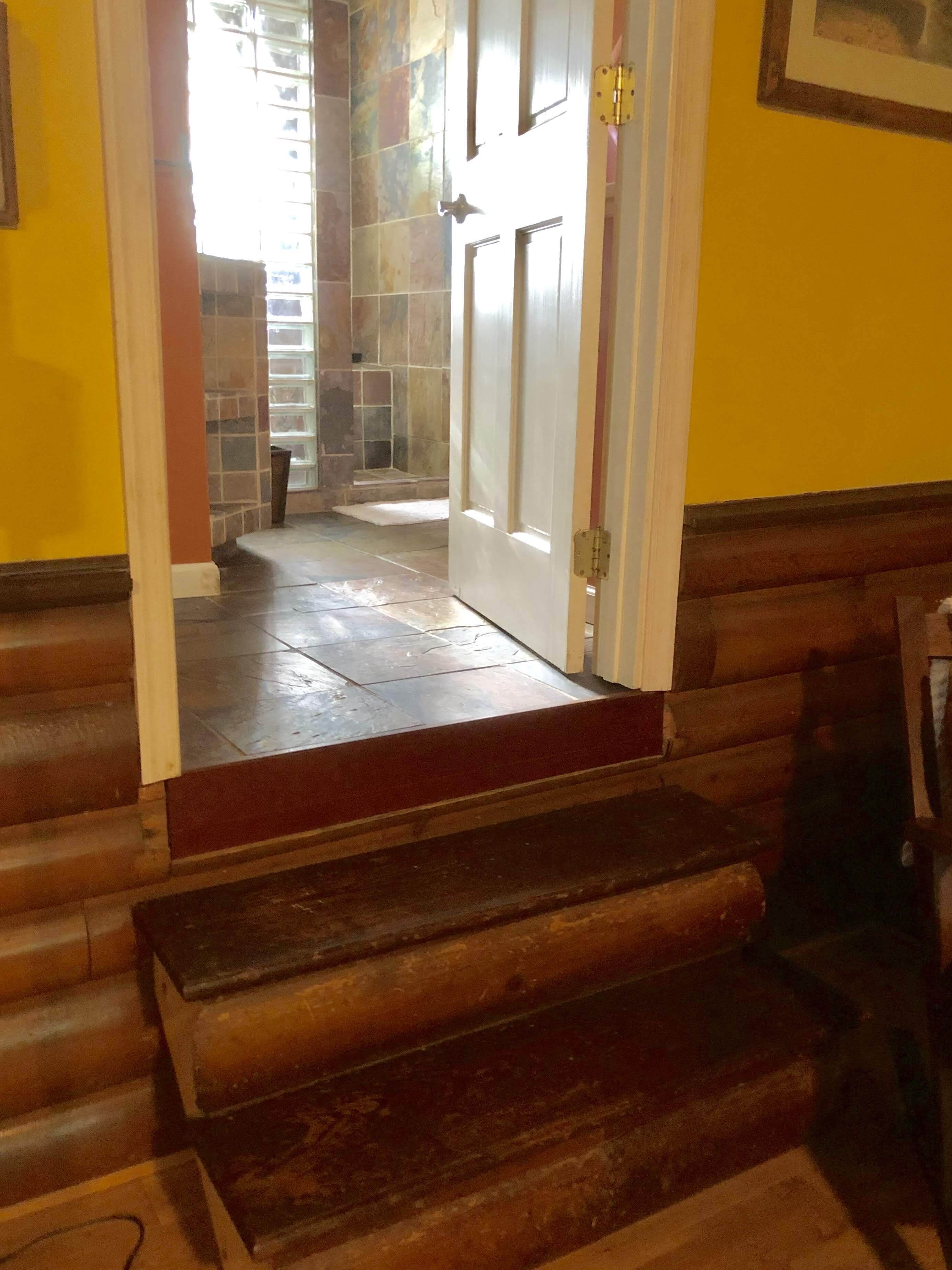 Eine Treppe führt zu einem Raum mit Duschbereich und einer Tür mit goldener Klinke.