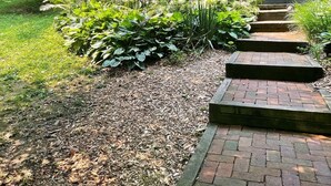 Un sendero en un jardín que lleva a una cabaña de madera con un porche cubierto.