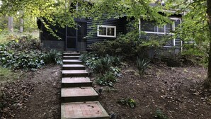 Una cabaña de madera con un ventanal pequeño y una escalera de piedra que lleva a la entrada.