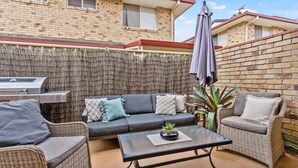 An outdoor patio with a sofa, chairs, a table, a grill, and a pergola.