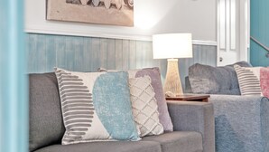 A living room with a grey sofa and multiple cushions, a lamp, and a wall-mounted picture.