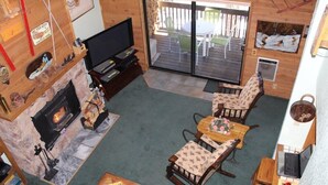 Een gezellige woonkamer met een open haard, houten meubels, een televisie en een schuifpui die leidt naar een terras.