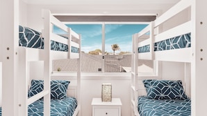 Una habitación con literas, una ventana con vista a un tejado con tejas y una palmera, y una mesita de noche con un adorno.